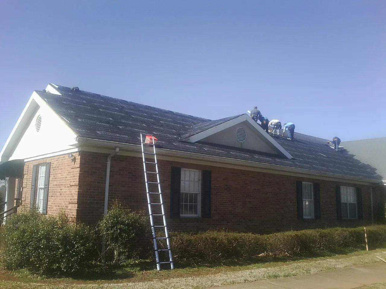 Crew tearing shingles off a brick ranch roof with a ladder set — Emergency Roof Repair work by our crew in Whiting