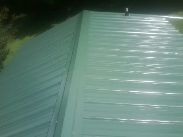 New green metal panels meeting at the ridge of a roof — Flat Roof Repair work by our crew in Whiting