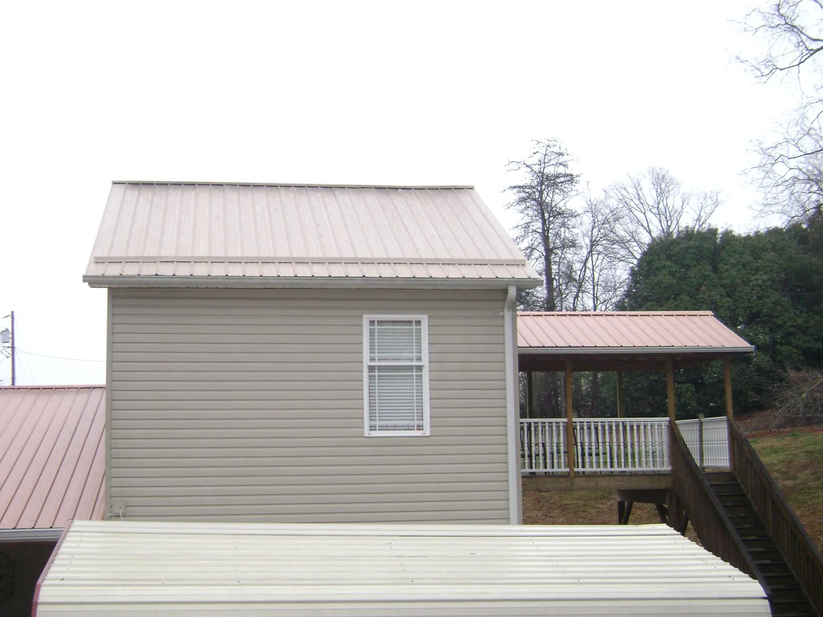 Tan metal roofs on a two story addition and attached porch, from a Roof Replacement job in Whiting